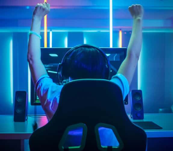 Ragazzo esultante di spalle mentre gioca a un video game in una stanza con vari neon blu